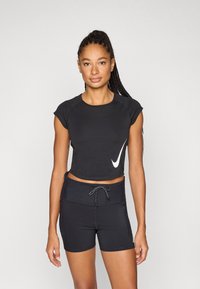 Čierny krátky atletický top s krátkymi rukávmi a bielym logom Nike, v kombinácii s čiernymi priliehavými šortkami so sťahovacou šnúrou a bočnými vreckami.
