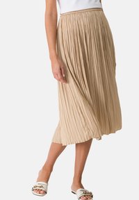 Gonna midi plissettata beige con elastico in vita e tessuto leggero, caratterizzata da pieghe profonde e una silhouette fluida.
