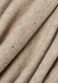 Beige gestrickter Stoff mit einem strukturierten Muster, das mehrfarbige Sprenkel in Gelb und Schwarz aufweist und sein weiches, gemütliches Aussehen betont.