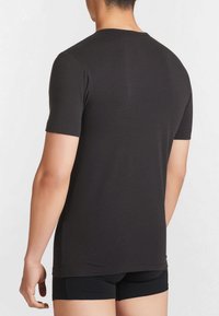 T-shirt in cotone nero con maniche corte, design a collo rotondo, texture liscia, forma aderente e orlo posteriore leggermente più lungo.