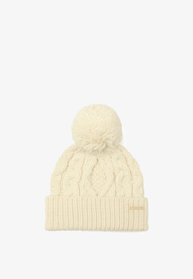 Gorro de invierno color crema, tejido, con patrón de trenzas, gran pompón en la parte superior y un borde de canalé doblado con una pequeña etiqueta de marca.