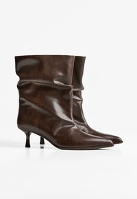 Bocanci până la gleznă cu textură maro asemănătoare unei snake, cu un design slăbuț, vârf ascuțit și toc mic de tip kitten. Finisaj neted cu o strălucire subtilă.