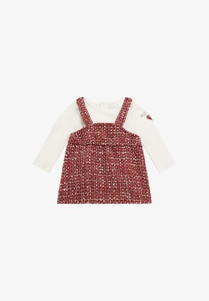Abito maglioncino intrecciato rosso e bianco con spalline su una maglietta bianca a maniche lunghe. Presenta un colletto rotondo e tessuto testurizzato.
