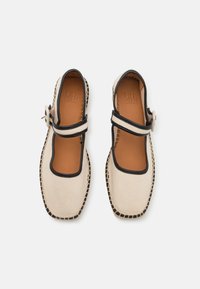 Beige canvas schoenen met zwart accent, vierkante neus en een Mary Jane bandje dat met een gesp is vastgemaakt. Natuurlijke leren binnenzool en zichtbare stiksels.