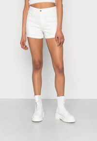 Calções de denim brancos com um design ajustado e uma textura suave, combinados com botas brancas até aos joelhos com atacadores e sola robusta.