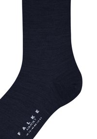 Navy plave čarape od teksturiranog materijala, sa glatkim završetkom i bijelom oznakom "FALKE AIRPORT" na gležnju.