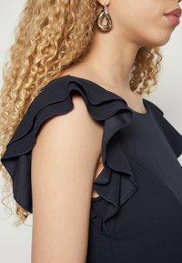 Mekko, jossa on tummansinihihnan rypytetty olkapäätiedot, valmistettu sileästä kankaasta, esittelee tiukan muotoilun ja pyöreän pääntien.