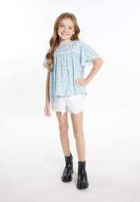 Himmelbluse mit Blumenmuster, kurzen, lockeren Ärmeln und Spitzenrand; kombiniert mit weißen, ausgefransten Shorts und schwarzen Stiefeletten. Schlicht, lässiger Schnitt.