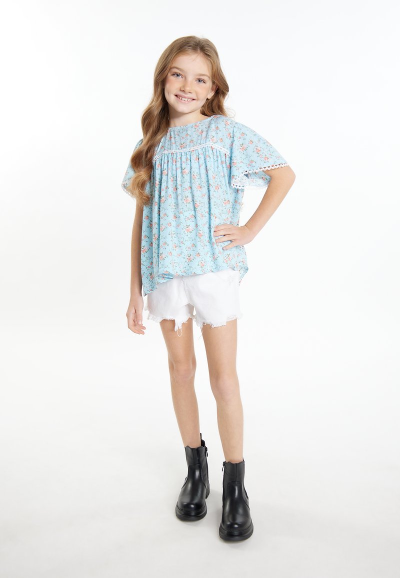 Himmelbluse mit Blumenmuster, kurzen, lockeren Ärmeln und Spitzenrand; kombiniert mit weißen, ausgefransten Shorts und schwarzen Stiefeletten. Schlicht, lässiger Schnitt.