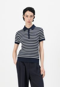 Jūrininkų dryžuota polo marškinėliai su trumpomis rankovėmis, pintos tekstūros ir apykakle; turi kontrastuojančius baltus dryžius ir keturis mygtukus priekyje.