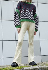 Strikket sweater i navy med røde prikker og zigzag-mønster, parret med beige brede teksturerede bukser og sorte sneakers.