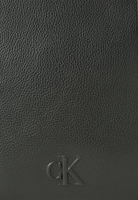 Schwarze Lederbörse mit strukturierter Oberfläche und geprägtem "ck"-Logo auf der Vorderseite. Einfaches Design ohne sichtbare Verschlüsse oder Fächer.