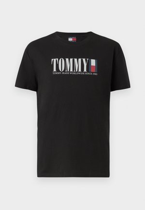 Crna pamučna majica s kratkim rukavima, sa velikim "TOMMY" logotipom u bijeloj boji i šarenim prugama. Okrugli izrez, glatka tekstura.