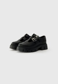 Chaussures noires avec une semelle plateforme épaisse et un design découpé, dotées de deux boucles latérales et de coutures décoratives sur la tige.