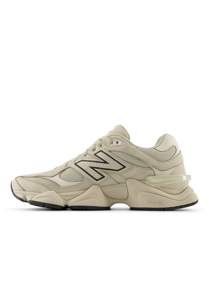 Chaussure de sport beige avec tige en mesh et cuir, arborant un logo noir, des accents texturés, et une semelle extérieure épaisse avec des détails subtils d'amorti.