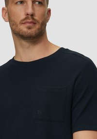 Marineblaue kurzärmlige T-Shirt aus Rippstoff, mit einer Brusttasche mit dezentem Branding und Rundhalsausschnitt.
