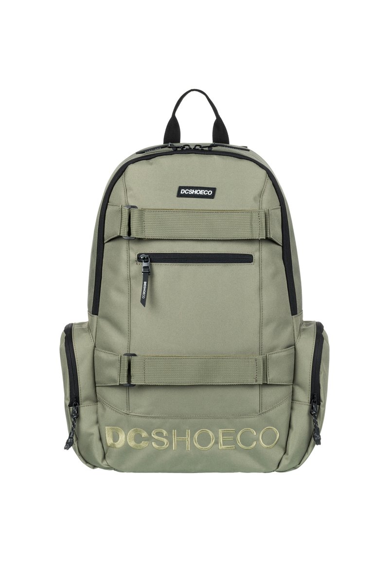 Mochila de tela verde con acentos negros, múltiples compartimentos con cremallera y correas ajustables. Presenta el logo "DCSHOECO" en dorado.