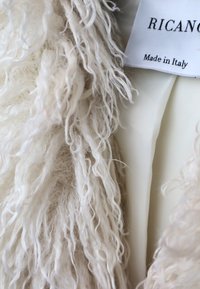 Wit, schapenvachtstof met een lange, krullende textuur naast een glad, crème-kleurig materiaal; etiket leest "RICAN" met "Made in Italy."