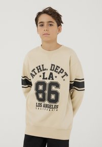 Felpa beige con testo grafico nero che recita "ATHL. DEPT. LA 86" e "LOS ANGELES CALIFORNIA." Presenta strisce nere sulle maniche.