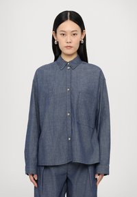 Denim srajca s gumbi v temno modri barvi, dolge rokave, žep na blazini in zaobljeno spodnje robove v sproščenem kroju.