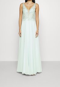 Dlouhé mátově zelené večerní šaty s výstřihem do V a zdobeným živůtkem. Obsahují volnou sukni a složité korálkování podél výstřihu.