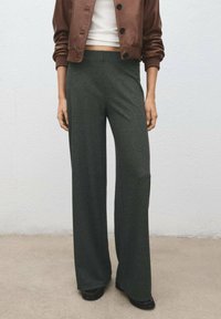 Vida byxor i texturerat mörkgrönt tyg, med en åtsittande midja och subtila detaljer, tillsammans med en brun kort jacka.