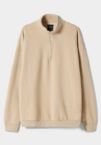Suéter de tejido suave en color beige, con cuello alto, cierre de media cremallera y puños acanalados. Ajuste relajado y diseño minimalista con una textura suave.