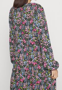 Musta mekko, jossa on kukkakuosi vaaleanpunaisen, sinisen ja vihreän sävyissä. Pitkät puffihihat ja kerätty vyötäröluettelo luovat vaihtelevaa siluettia.