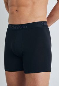 Boxers noirs en tissu lisse, dotés d'une large ceinture avec le logo Calvin Klein en gris. Coupe ajustée avec une longueur mi-thigh.
