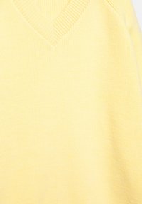 Weicher gelber Strickpullover mit V-Ausschnitt und geripptem Rand am Kragen, aus feinem, gemütlichem Stoff gefertigt.