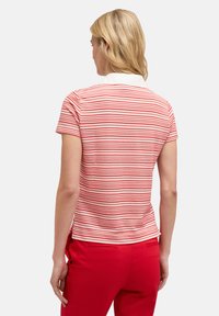 Polo de rayas rojas y blancas con cuello blanco, mangas cortas y un diseño ajustado, combinado con pantalones rojos.