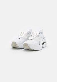 Vita sneakers i mesh och syntetiska material, med en texturerad yta, kontrasterande svarta detaljer och en tjock, vadderad sula.