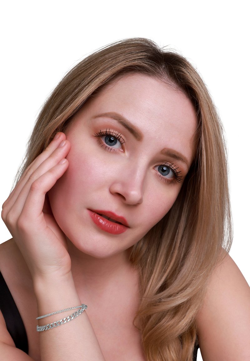 Primo piano di una persona con lunghi capelli biondo chiaro, pelle chiara e un sottile braccialetto d'argento. Texture della pelle liscia, trucco leggero con labbra di un rosso tenue.