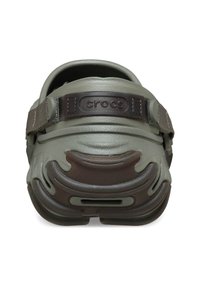 Grijze Crocs met een donkerbruine band, met een gestructureerd oppervlak en ventilatiegaten. De merknaam "crocs" is zichtbaar aan de achterkant.