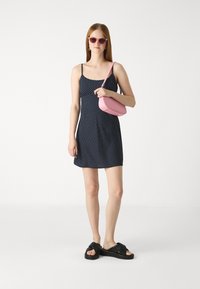 Morska haljina s polka točkicama, kratka, s tankim naramenicama, uparena s crnim klompama i ružičastom crossbody torbom. Glatka tkanina, opušteni kroj.