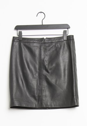 Mini-jupe en cuir noire suspendue à un cintre en plastique noir sur fond blanc.