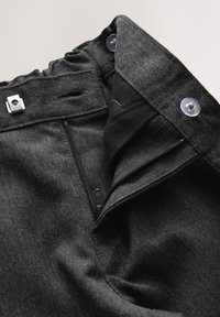 Pantalon gris foncé avec fermeture éclair ouverte, bouton pression et taille ajustable avec tissu élastique froncé.