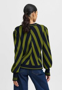 Pull en tricot ornée de rayures diagonales vertes et bleu marine, col rond, manches bouffantes et ourlet côtelé. Texture douce avec un poids moyen.
