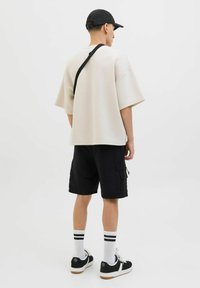 Przeciętny beżowy T-shirt z krótkim rękawem, zestawiony z czarnymi szortami cargo, białymi sportowymi skarpetkami i czarnymi trampkami z białymi akcentami.