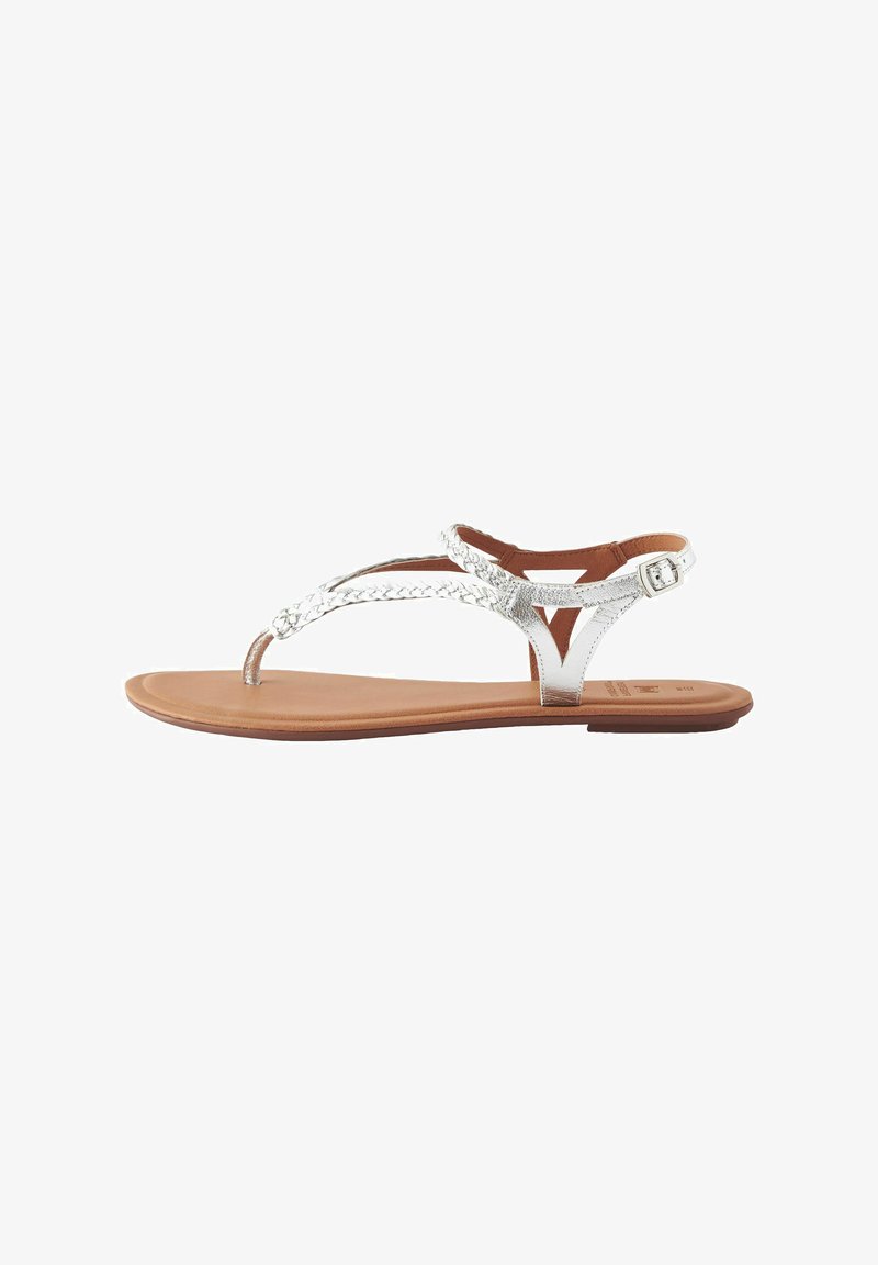 Sandali thong metallici argento con cinturini intrecciati, suola piatta marrone e fibbia regolabile alla caviglia per una vestibilità sicura.