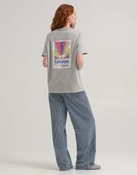 Maglietta in cotone grigia con una grande grafica colorata ispirata al retrò sul retro, abbinata a pantaloni a gamba larga blu a righe.