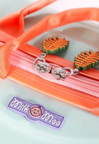Orange zippered pouch with two carrot-shaped zipper pulls and a purple label featuring a smiling baby face and the words "Milk Mama."