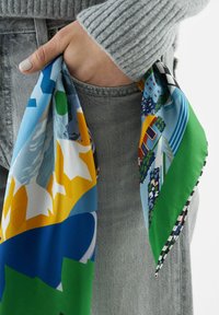 Écharpe en soie multicolore présentant des motifs géométriques, des montagnes, des arbres et des bâtiments. Les bords sont bordés d'un design à damier noir et blanc.