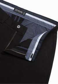 Svarta byxor med öppen dragkedja och knapp, som visar ett mönstrat blått innerfoder och varumärkesetikett "ombre Quintessence" storlek M 32.