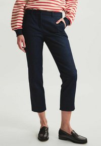 Pantalons cropped en denim bleu foncé, avec une coupe plate à l'avant, des poches latérales et une ceinture assortie, associés à des mocassins marron.