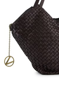 Ciemnobrązowa torebka z plecionki skórzanej o gładkiej fakturze. Posiada ozdobny mosiężny charm w kształcie symbolu pokoju, przymocowany łańcuchem.