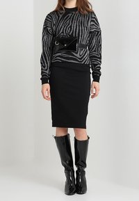 Schwarzer und grauer, zebra-gestreifter Pullover, schwarzer, taillierter Rock, schwarze, glänzende Knielange Stiefel und eine schwarze, glänzende Gürteltasche mit Klappe.