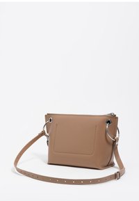 Beżowa skórzana torba na ramię o prostokątnym kształcie, z akcentami w postaci srebrnych pierścieni, zamkiem błyskawicznym i zewnętrzną kieszenią. Dołączony regulowany pasek.