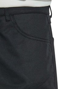 Dunkelgraue Jeanshose mit einer Vordertasche, sichtbaren Nähten und einer glatten Textur. Der Stoff weist einen leichten Glanz auf.