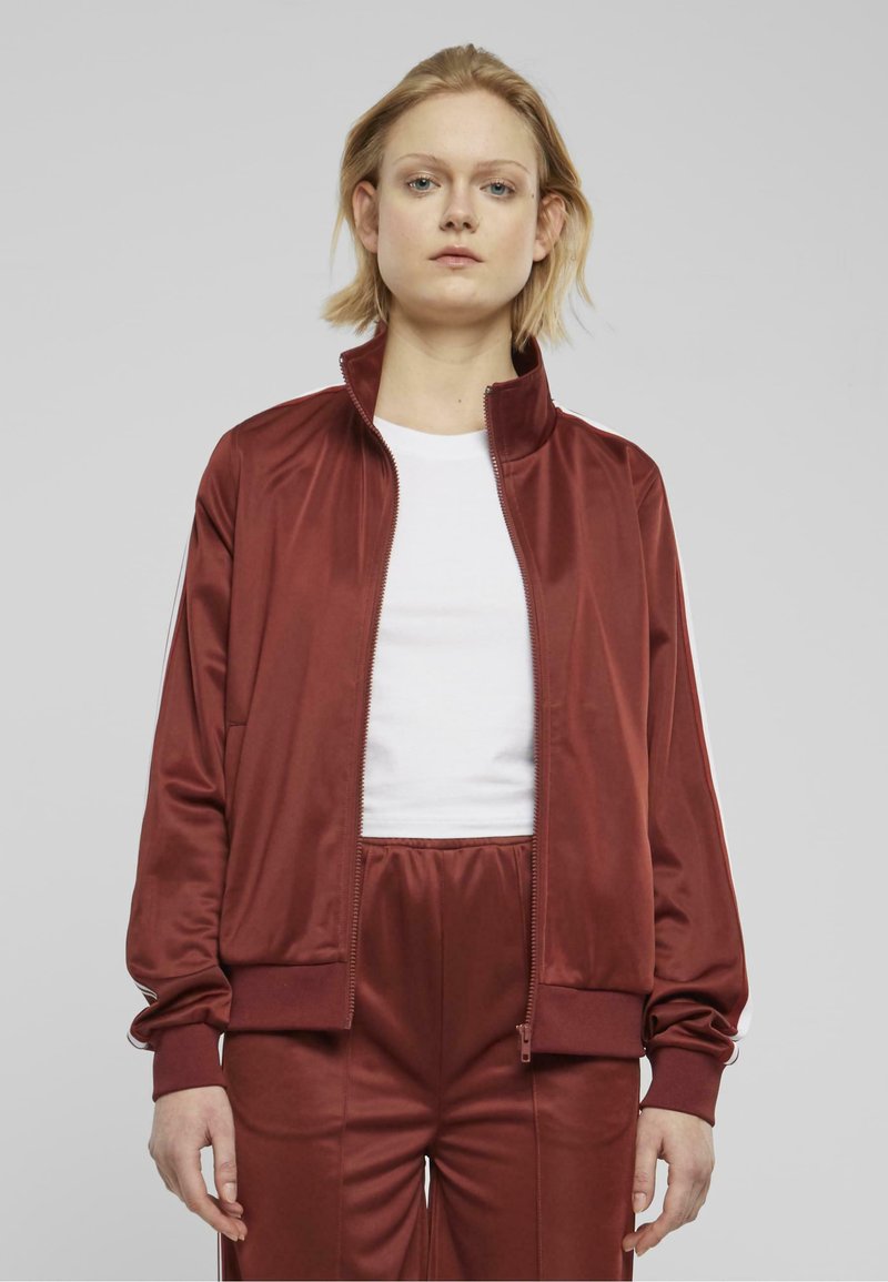 Burgundy treen takki, jossa on vetoketjullinen etuosa, korkea kaulus ja valkoiset sivuraidat. Kapea malli, jossa on sileä, kiiltävä kangas ja elastiset hihansuut.
